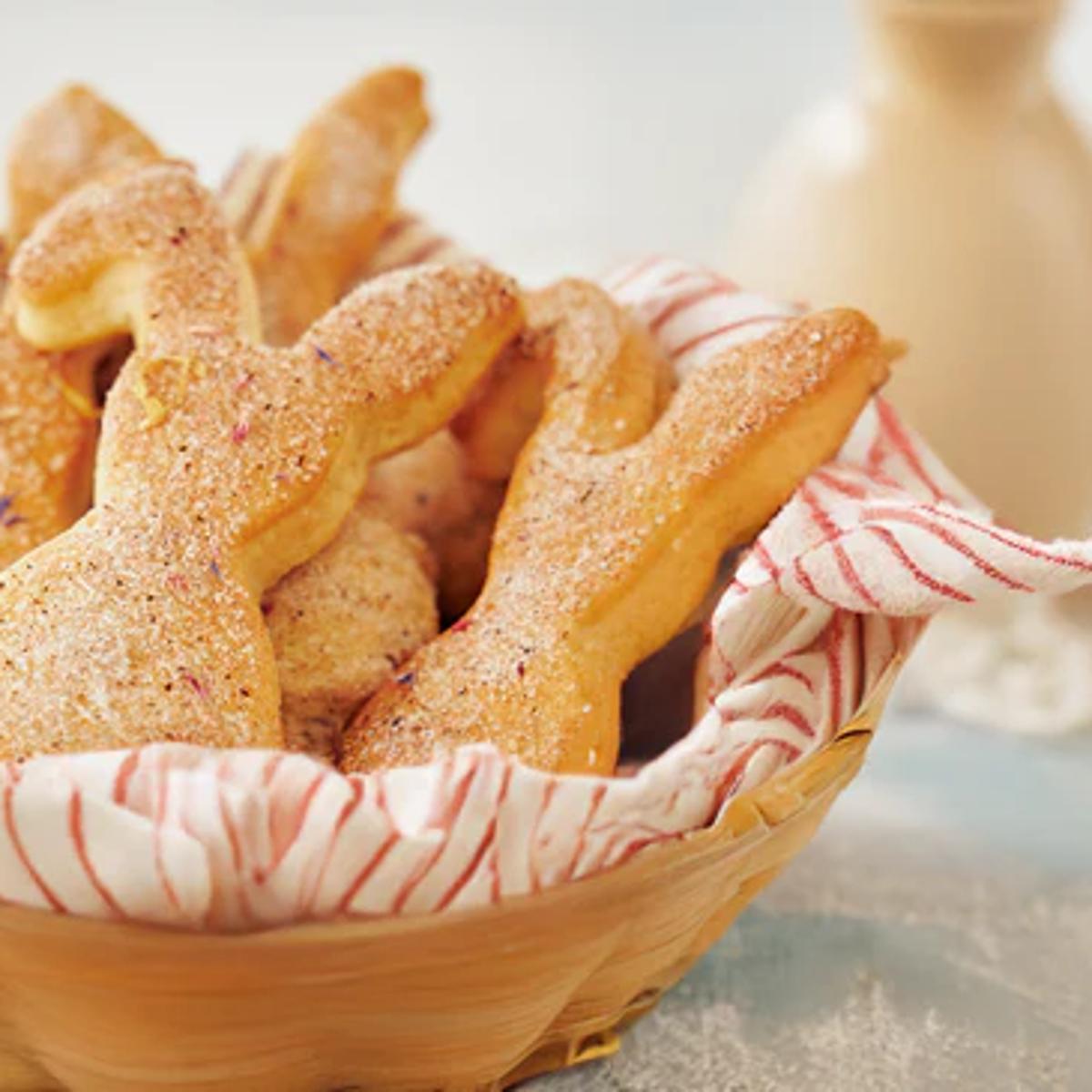 Osterhasen-Plätzchen mit Vanillezucker und Blütenmischung in einem geflochtenen Brotkorb mit rot-weißem Tuch, serviert auf hellem Ostertisch